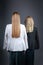Two girls with long blond hair stand against wall in strict suits, rear view