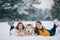 Two girls are lying in snow next to a dog Alaskan Malamute and hugs his