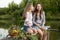 Two girls in plaid shirts sit on a bridge on a pond and laugh