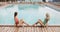 Two girls posing by the hotel pool. Young womans in a one piece swimsuit sitting on the edge of a swimming pool, posing