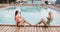 Two girls posing by the hotel pool. Young womans in a one piece swimsuit sitting on the edge of a swimming pool, posing