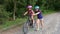 Two girls in protective bicycle helmets in the summer in the park. The older sister helps the younger one learn to ride a bicycle