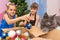 Two girls pull Christmas toys out of the box and show the cat