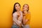 Two girls send kiss to social friends. Emotional and joyful expression. Yellow background