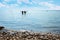 Two girls silhouettes in the water, gravel beach and blue sky with clouds