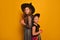 Two girls sisters dressed up as Halloween witch on yellow background. Kids looking up and holding red lighted candles.