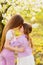 two girls sisters have fun and cuddle in the garden with flowering trees.