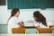 Two girls sit at school desks and look toward blackboard