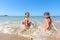 Two girls sit on the sea coast and turn around happily looking at the frame