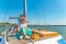 Two girls sit on a yacht on the deck near the mast and look out into the sea.