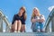 Two girls sitting on metal bridge with blue sky