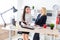 Two girls stand in the office near the table and look at each other.