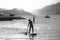 Two girls stand up paddle paddling alongside boats moored at Guaruja beach