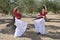 Two girls in a symmetrical position practicing flamenco with a skirt on the fly in an olive grove