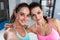 Two girls taking selfie wearing sports bra indoors. Close-up shot of female athletes smiling at camera hugging each
