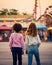 Two girls with their backs to the camera looking at an amusement park. Generative AI