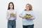 Two girls, thick and thin, with healthy food from vegetables and fruits and unhealthy fast food with a hamburger. The