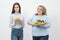 Two girls, thick and thin, with healthy food from vegetables and fruits and unhealthy fast food with a hamburger. The