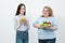 Two girls, thick and thin, with healthy food from vegetables and fruits and unhealthy fast food with a hamburger. The