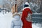 Two girls walking along the winter snowy street of the city, children are holding hands, back view