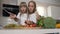 Two girls in white dresses are cutting vegetables at home in the kitchen. Two charming girls preparing salad. Attractive