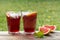 Two glasess with grapefruit drinks, wooden table, green garden background