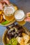 Two glass of beer in hand. Beer glasses clinking in bar or pub on table with food background