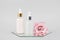 Two glass bottles with serum, essential oil or other cosmetics product and beautiful pink flowers on mirror on grey