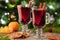 Two glass of christmas mulled wine or gluhwein with spices and orange slices on rustic table against the Christmas tree.
