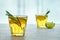 Two glass cups of kombucha are decorated with rosemary and lemon against the background of silhouettes of bamboo trees