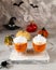 Two glass cups of pumpkin juice with painted faces on the background of Halloween pumpkins on a gray wall with ghosts