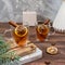 Two glass cups of tea with lemon, close-up of cinnamon sticks on a wooden table on a Christmas background. Warm healing