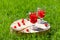 Two glass glasses with cherry and water stand on a wooden stand with a crack on the green lawn on a summer day