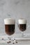 Two glass glasses with handles with Irish coffee with coffee beans on a wooden table