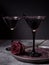 Two glasses with black cocktail, dried rose for Halloween party on the dark background