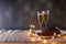 Two glasses of champagne, chocolate cake, glowing lights  and christmas decorations on table. Selective focus. View with copy