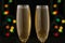 Two glasses with champagne with festive lights on a dark background