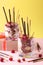 Two glasses with chocolate granola, banana and raspberry, decorated with sticks Pocky on yellow and pink background. Vertical