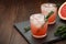 Two glasses of citrus summer drink with grapefruit and rosemary on dark background.