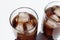 Two glasses of cola with ice cubes on white table. Top view, copy space. Hard light, shadow.  Refreshing summer drink