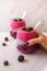 Two glasses filled with layered Blueberry Raspberry smoothie & almond milk chia pudding with silver spoons against white backgroun