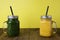 Two glasses with green and yellow detox smoothie with straws. Spinach and pumpkin smoothie on wooden table. Copy space