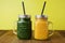 Two glasses with green and yellow detox smoothie with straws. Spinach and pumpkin smoothie on wooden table and yellow