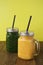 Two glasses with green and yellow detox smoothie with straws. Spinach and pumpkin smoothie on wooden table and yellow backgraund