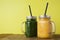 Two glasses with green and yellow detox smoothie with straws. Spinach and pumpkin smoothie on wooden table and yellow backgraund