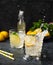 Two glasses of Lemonade drink with fresh lemon and splashes. Refreshing cocktails with lemons, mint and ice on dark background.