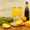 Two glasses of mimosa cocktail, a bottle of champagne, fresh oranges, mimosa sprig on a wooden table