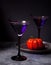 Two glasses with purple cocktail, dried roses, pumpkin for Halloween party on the dark background