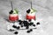 Two glasses of red juice and white ice, silvery spoon, drinking straws, mint, blackberries on a light gray background.