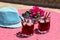 Two glasses of summer red cocktail with ice next to a book, a sprig of Bougainvillea flowers, blue hat on a pink table